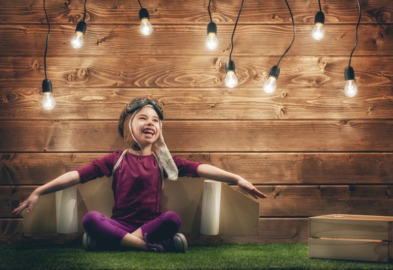 Little child girl plays astronaut. Child on the background of wooden wall. Child in an astronaut costume plays and dreams of becoming a spaceman.